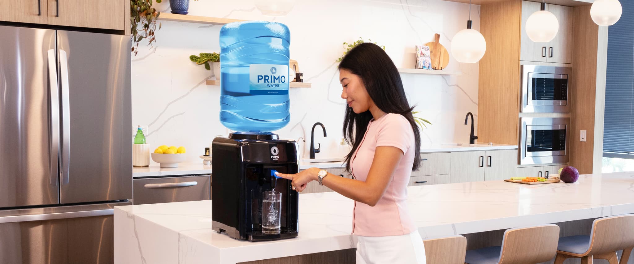Woman using a countertop water dispenser in a modern kitchen with wood cabinets and stainless steel appliances.