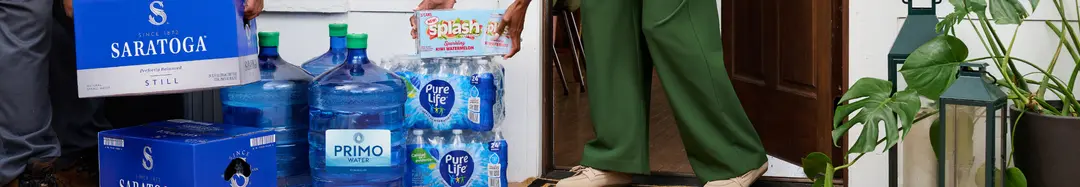 Person carrying bottled water and bulk jugs into a house after delivery.