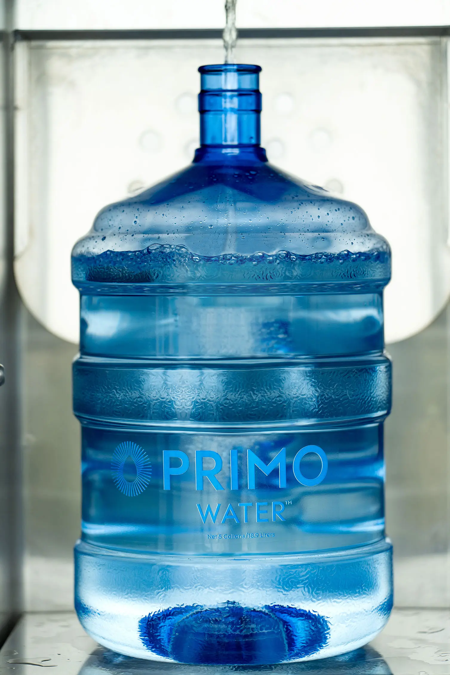 A large blue water jug labeled "Primo Water" is being filled, with droplets visible on the surface.