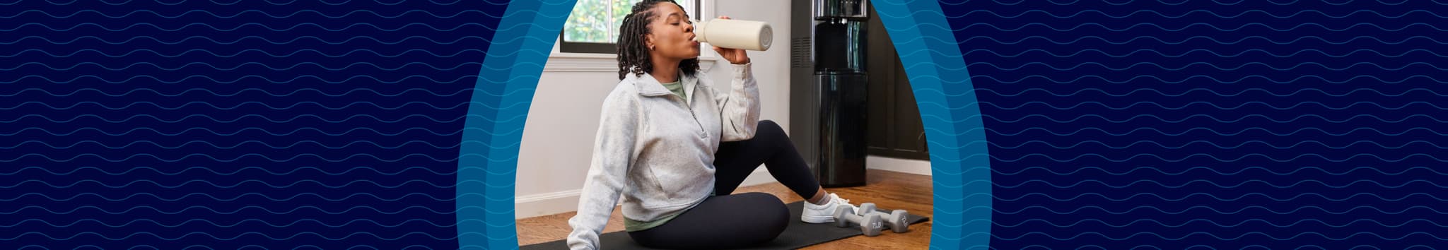 A woman in workout clothes sits on a mat indoors, drinking from a bottle, with a Primo water dispenser