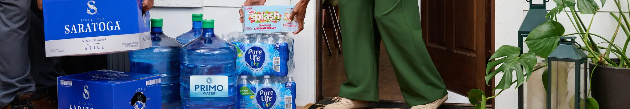 Person carrying bottled water and bulk jugs into a house after delivery.