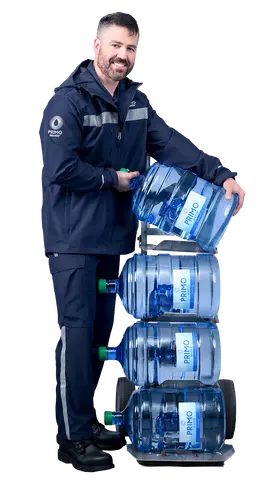 Man in a blue uniform smiling while stacking large water bottles labeled "Primo" on a dolly, standing against a white background.